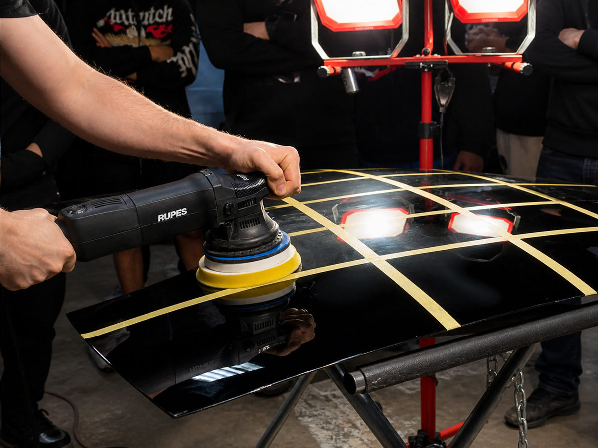Person using a Rupes car polisher on a black surface with lights in the background